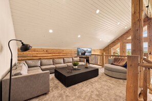 A cozy log cabin interior with a sectional sofa, a black coffee table, a TV, and a wooden railing.