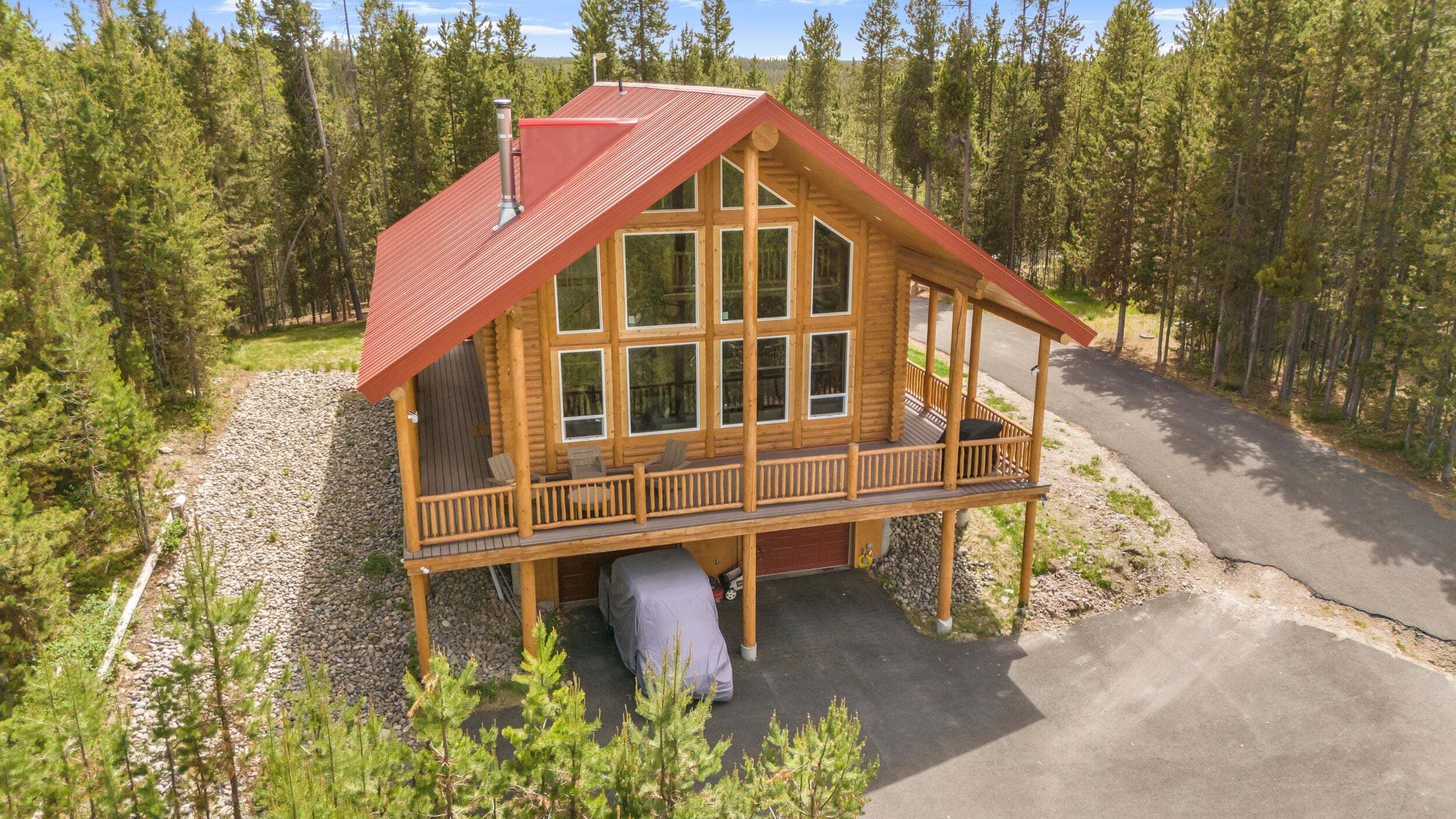 A log cabin with a red roof, large windows, and a porch.