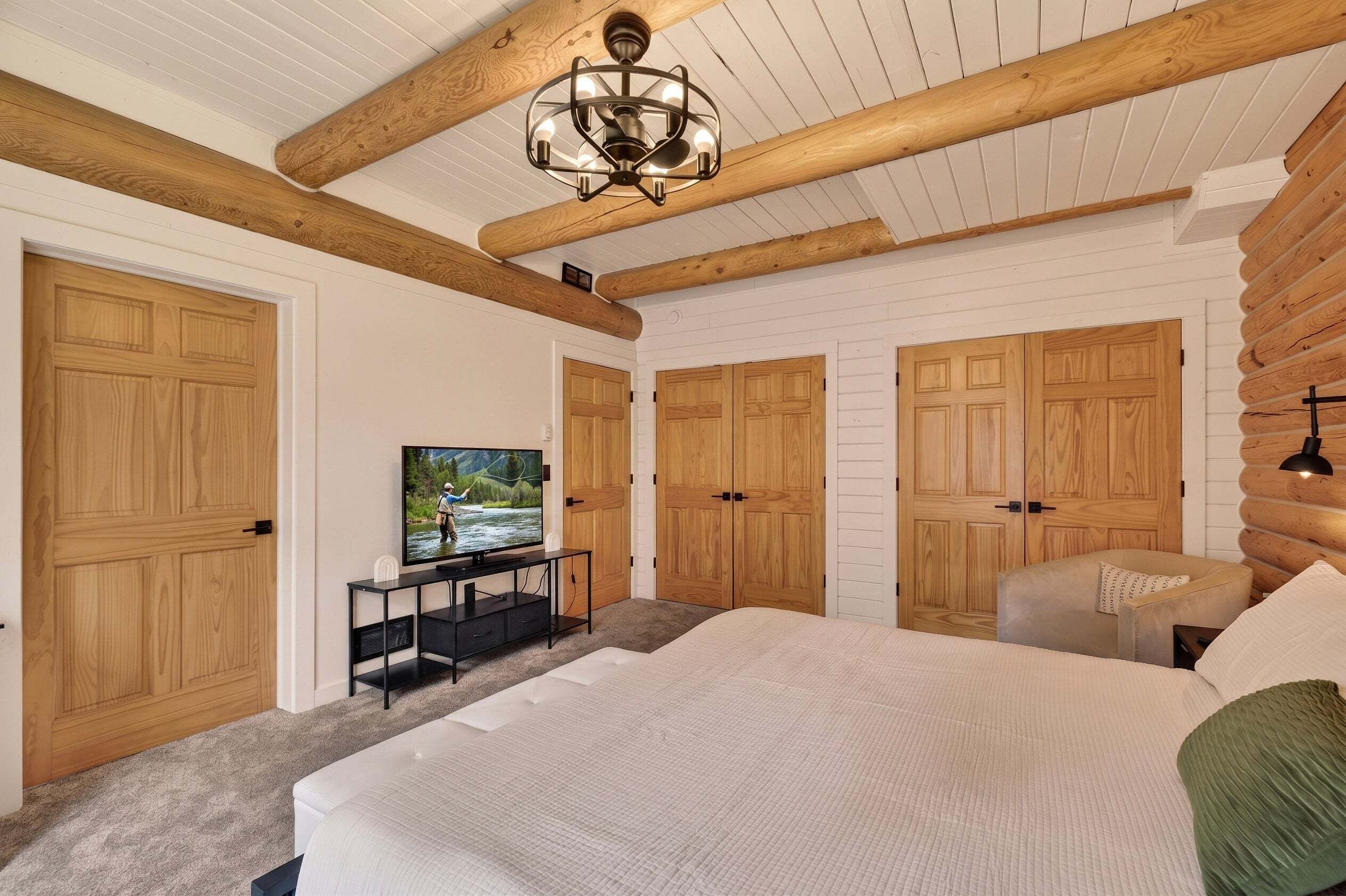 A bedroom with a large bed, wooden wardrobe, a television on a stand, and a wooden ceiling.