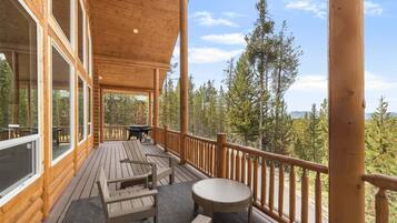 A wooden deck with outdoor furniture, large windows, and a view of trees.