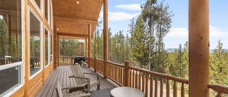 A wooden deck with outdoor furniture, large windows, and a view of trees.