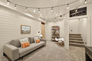 A room with a gray sofa, a small table, a staircase, and string lights.