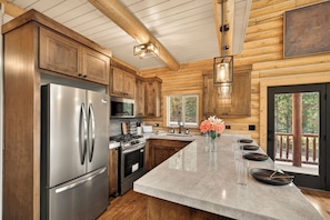 A modern kitchen with wooden cabinetry, stainless steel appliances, and a marble countertop.