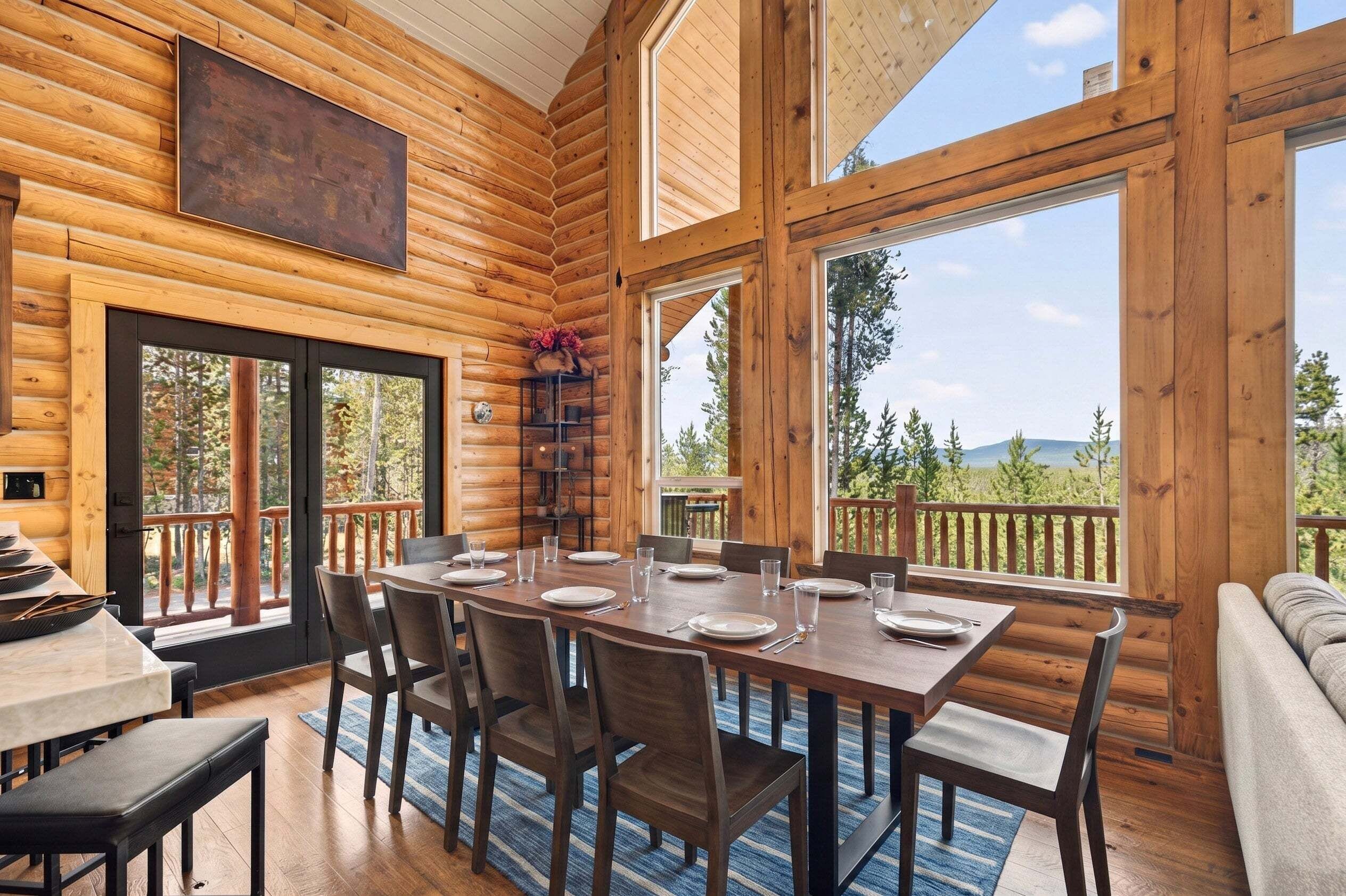 A log cabin interior with a dining area, large windows, and a view of the outdoors.