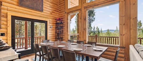 A log cabin interior with a dining area, large windows, and a view of the outdoors.