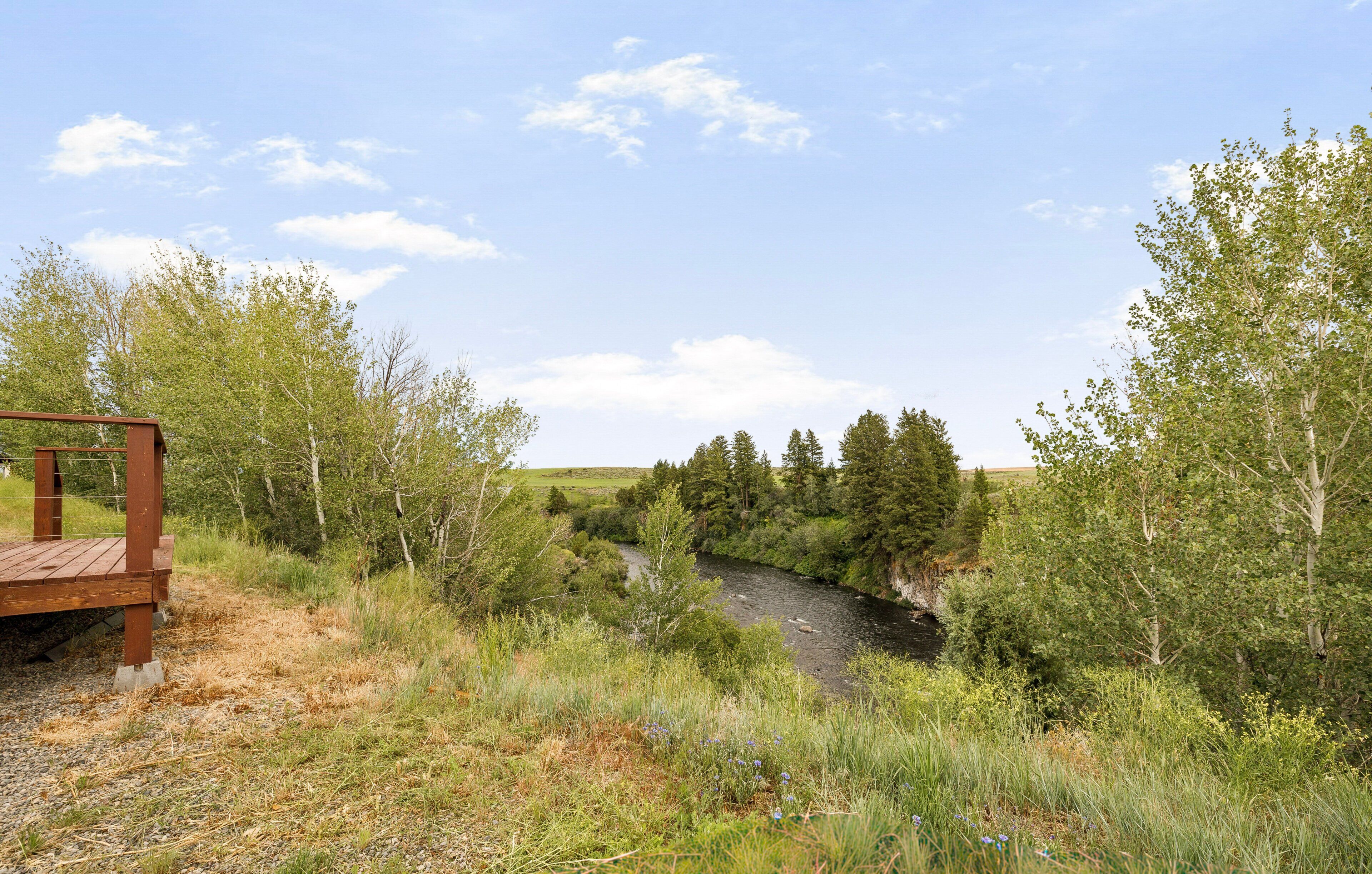 A wooden deck overlooking a river with trees and a clear sky.