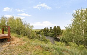 A wooden deck overlooking a river with trees and a clear sky. - The Hatch Cabin (Ashton)