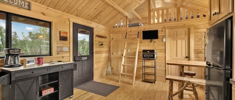 A wooden cabin interior with a kitchen, a dining area, and a sleeping loft.