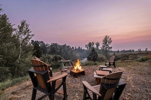 Un camping con una fogata, sillas de madera y vistas del paisaje circundante.