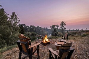 Un camping con una fogata, sillas de madera y vistas del paisaje circundante.