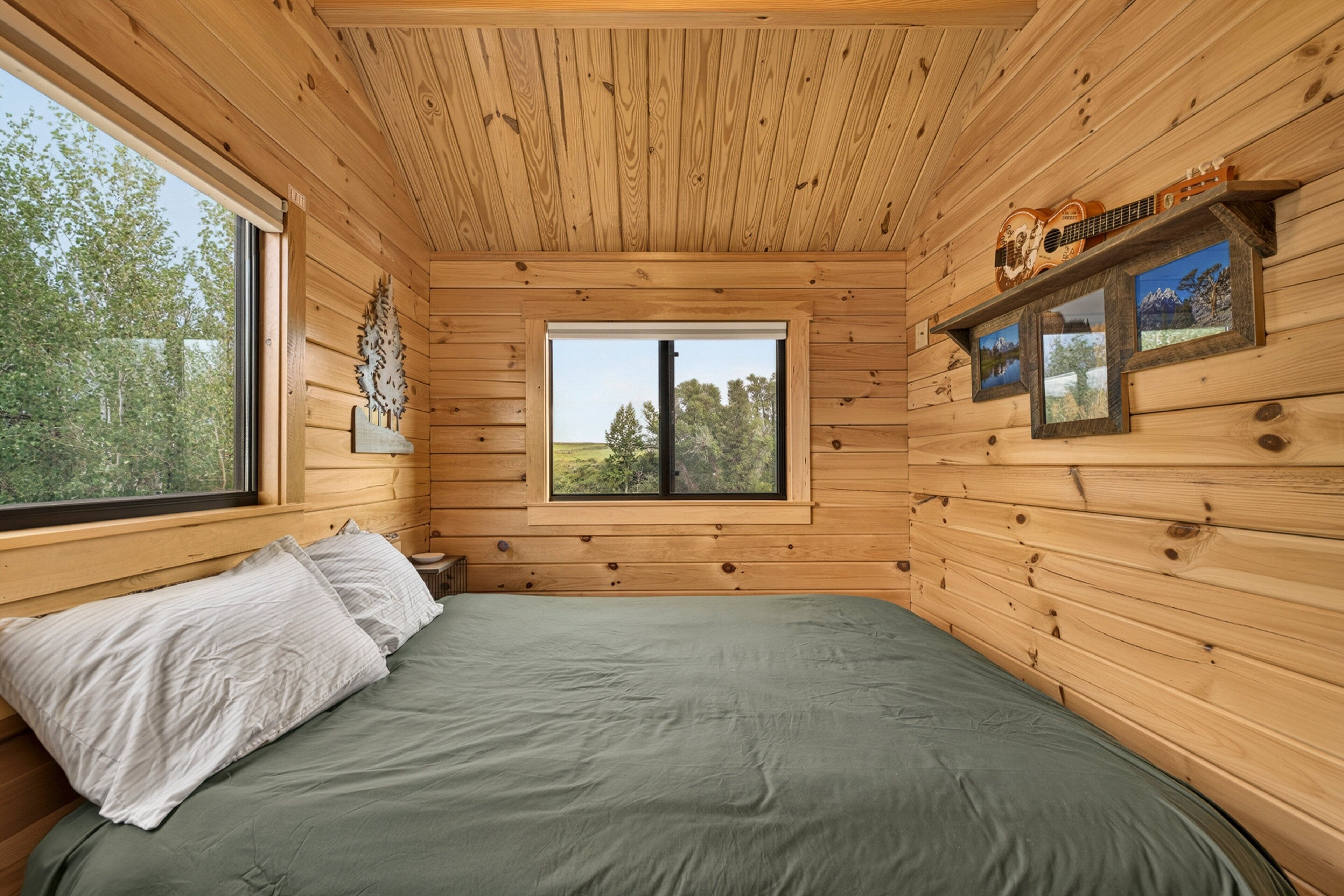 A wooden cabin room with a bed, a window, and a shelf with framed pictures.