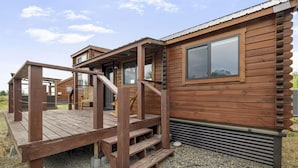 A wooden cabin with a porch, a staircase, and a window. - The Hatch Cabin (Ashton)