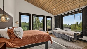 Een slaapkamer met een bed, een hangstoel en grote ramen met uitzicht op groen.