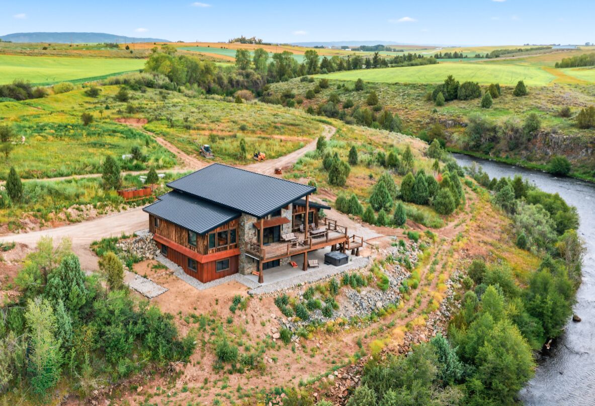 Una casa moderna con un'ampia terrazza, immersa in un paesaggio naturale con un fiume e campi.