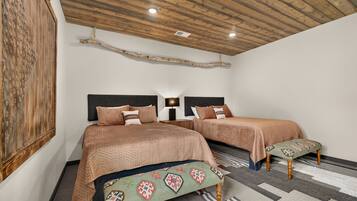 A bedroom with two beds, a wooden ceiling, a wall-mounted artwork, and a patterned rug.