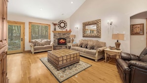 A spacious living room with a stone fireplace, two sofas, a leather armchair, and a large mirror. - Alpine Ascent (Alpine)