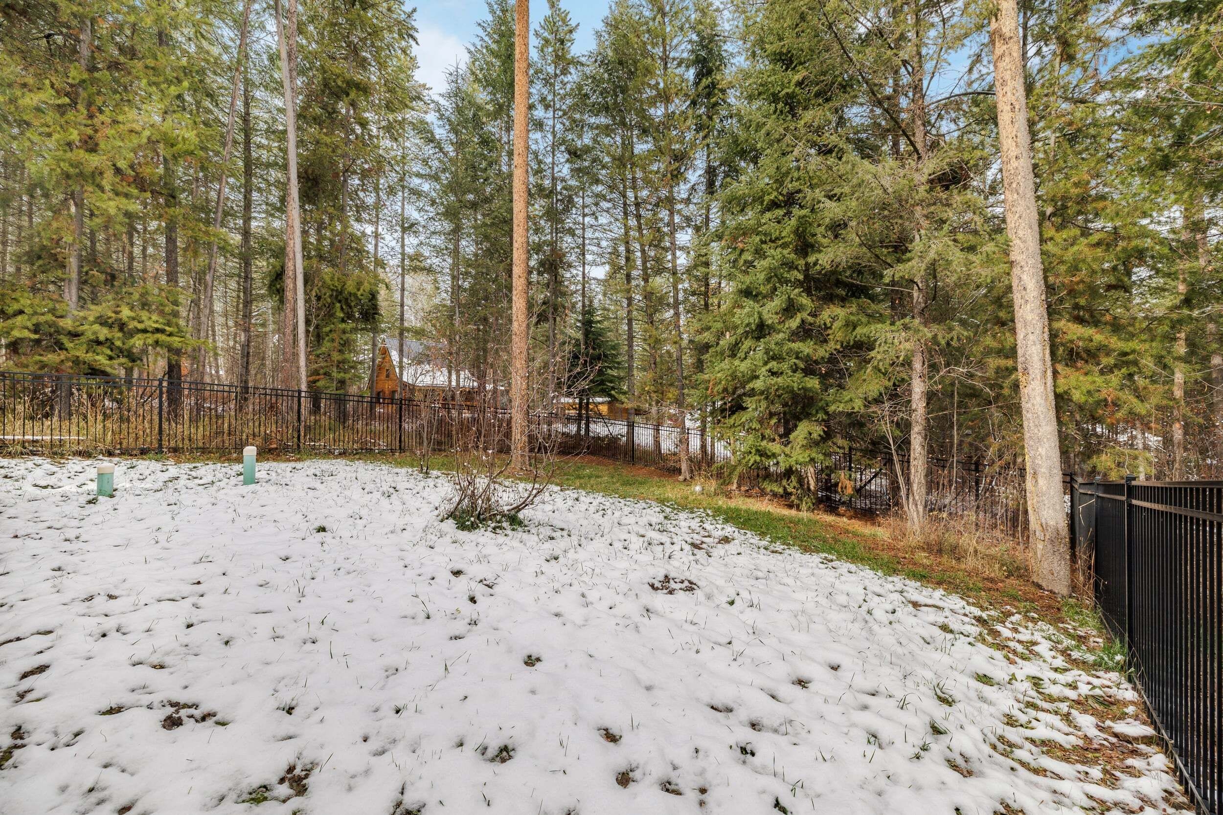 A snowy landscape with a fenced area, trees, and a building in the background.