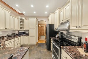 Une cuisine avec des meubles blancs, un réfrigérateur noir, une cuisinière et un four à micro-ondes.