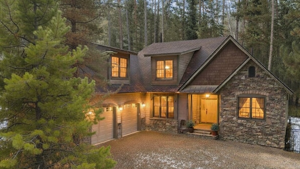 A two-story stone house with a stone exterior, a garage, and a gravel driveway. - Alpine Ascent (Alpine)
