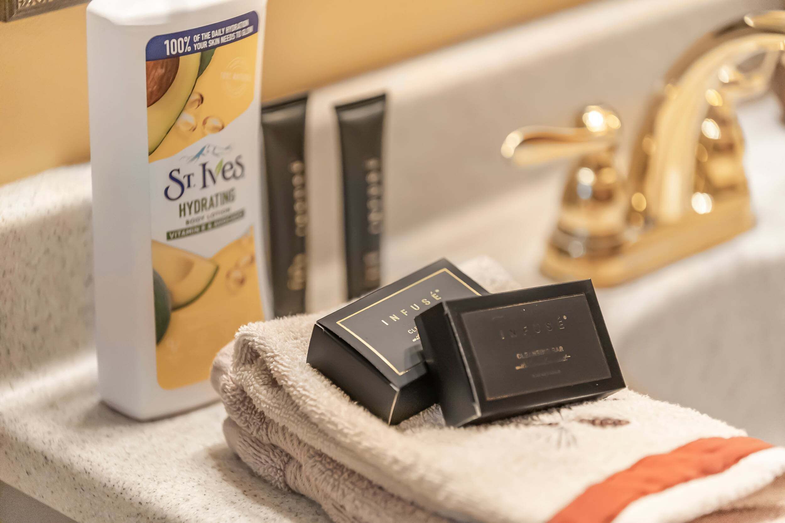 Un lavabo de salle de bain avec une bouteille de lotion hydratante pour le corps de la marque St. Ives, deux boîtes noires et une serviette.
