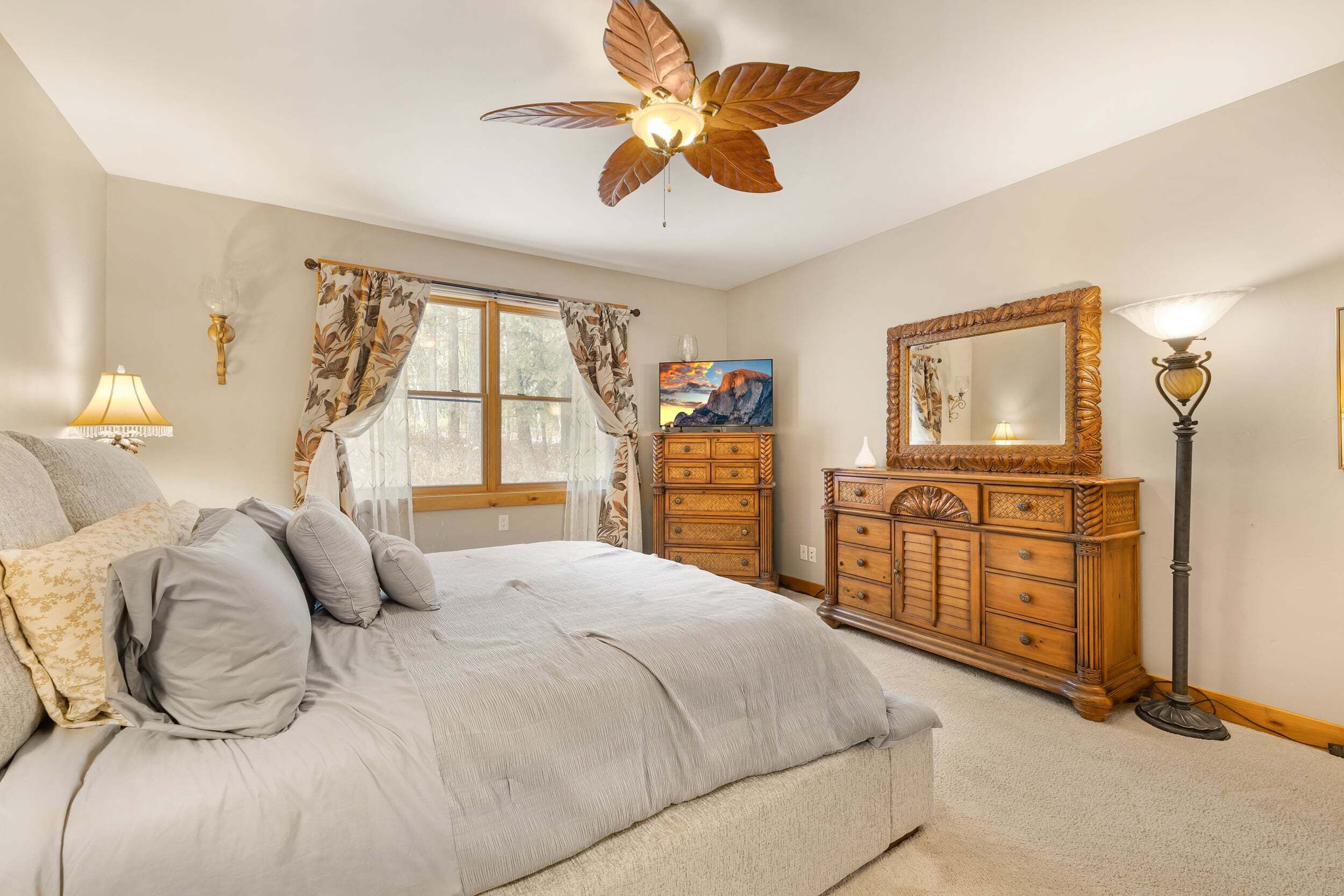 Ein Schlafzimmer mit einem Bett, einer Holzkommode, einem Deckenventilator, einem Gemälde und einer Lampe.