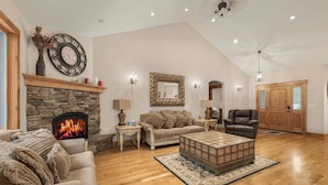 A spacious living room with a stone fireplace, a large clock, and a high ceiling with recessed lighting. - Alpine Ascent (Alpine)