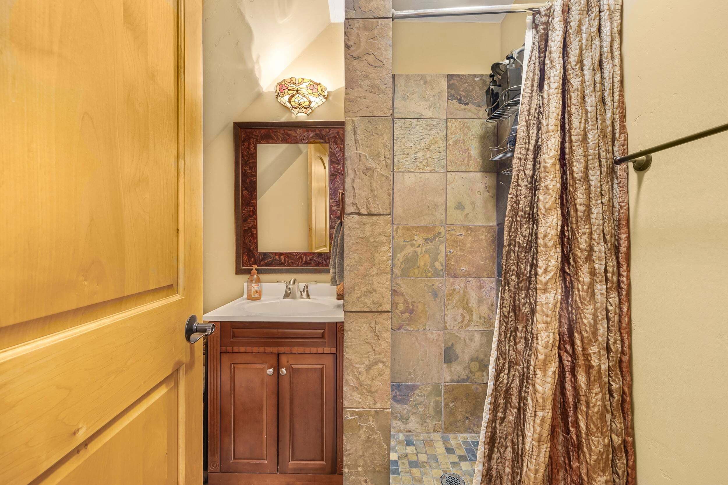 A bathroom with a wooden door, a sink with a mirror, and a shower curtain.