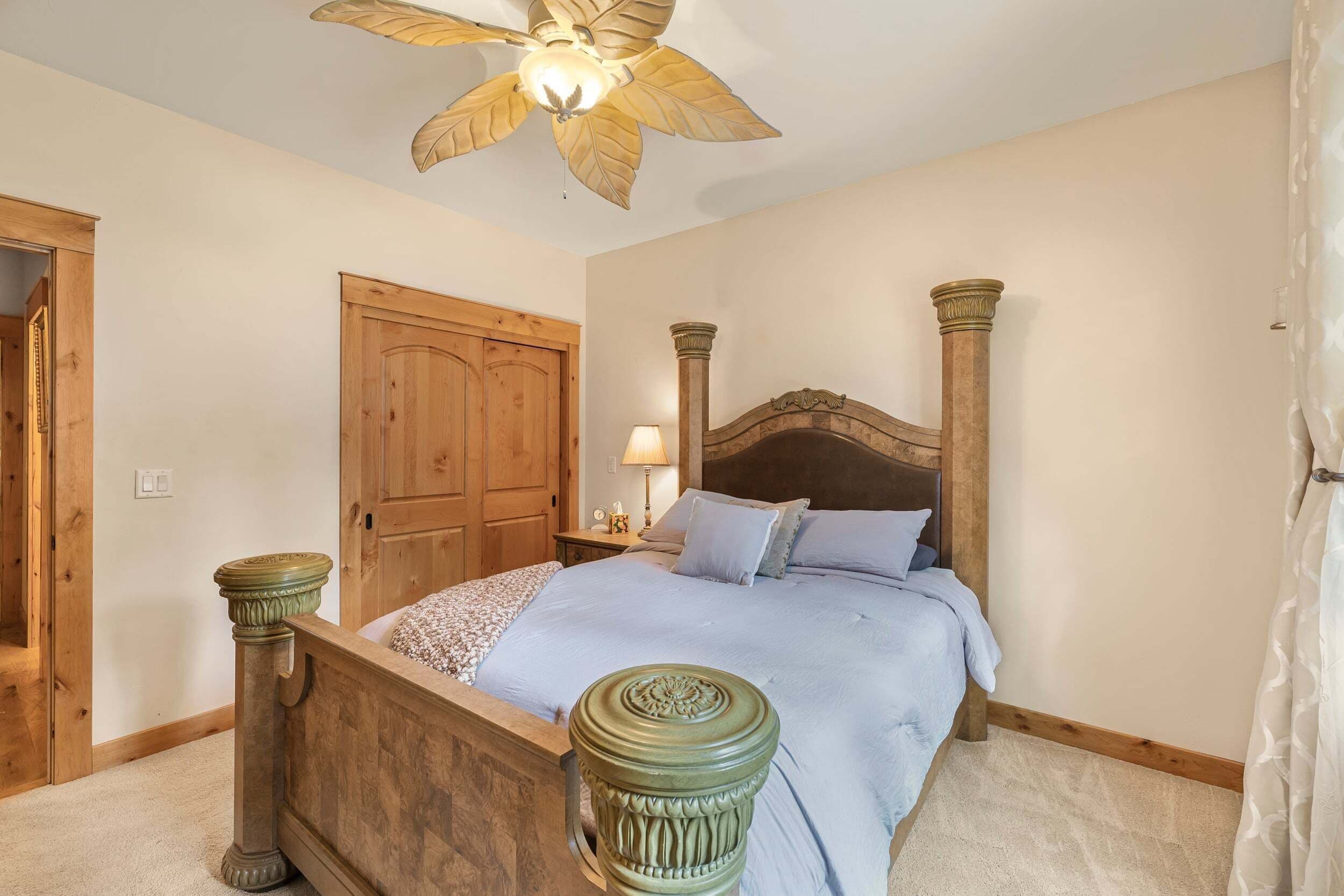 A bedroom with a wooden bed, a ceiling fan, a wooden wardrobe, and a nightstand with a lamp.