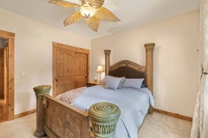 A bedroom with a wooden bed, a ceiling fan, a wooden wardrobe, and a nightstand with a lamp. - Alpine Ascent (Alpine)