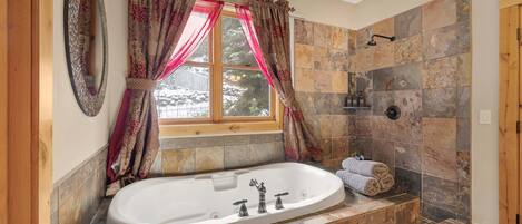 A bathroom with a freestanding bathtub, a window with curtains, and stone tiles.