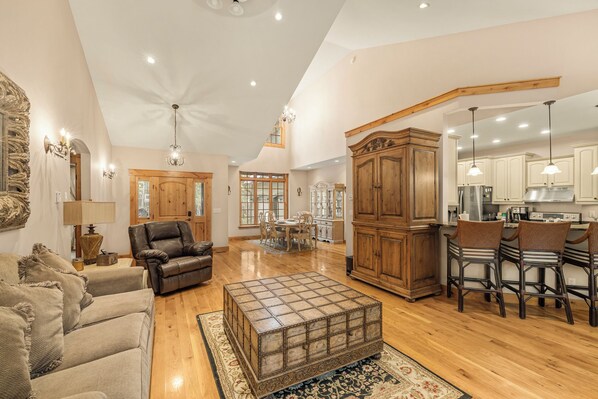 A spacious living room with a large wooden coffee table, leather sofas, and a dining area with wooden chairs.