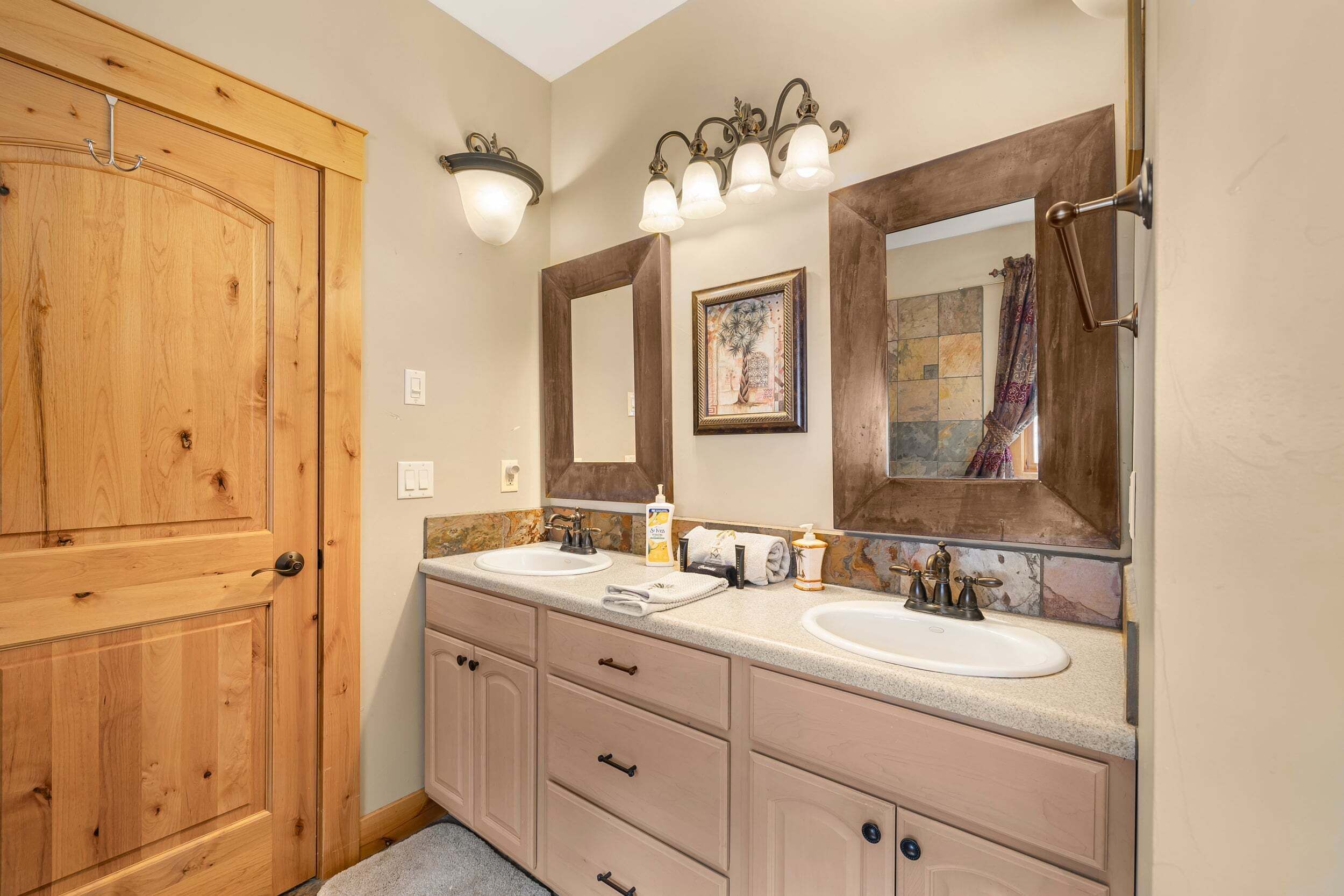 A bathroom with wooden cabinetry, two sinks, a large mirror, and wall-mounted lighting.