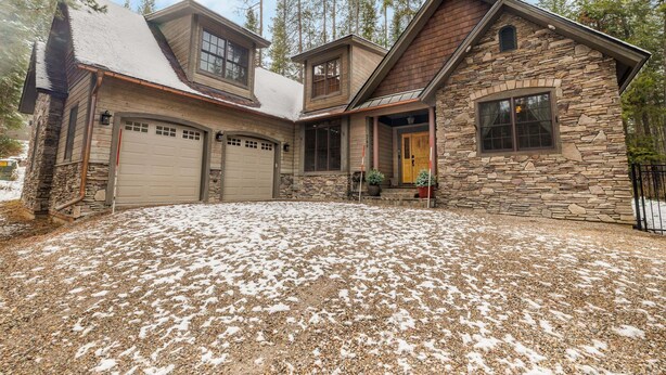 A two-story stone house with a garage, a stone exterior, and a gravel driveway.