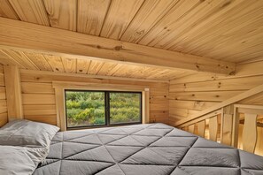 A wooden cabin bedroom with a bed, a window, and a view of greenery outside. - Eagles Nest Cabin (Ashton)