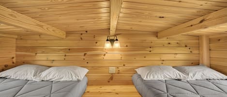 A cabin with two beds, wooden walls, and a ceiling with exposed beams.