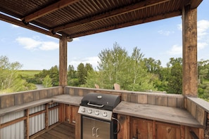 Cocina al aire libre con parrilla, terraza de madera y vista a un río y bosque.