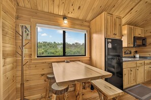 A wooden cabin interior with a large window, a dining table, and a refrigerator. - Eagles Nest Cabin (Ashton)
