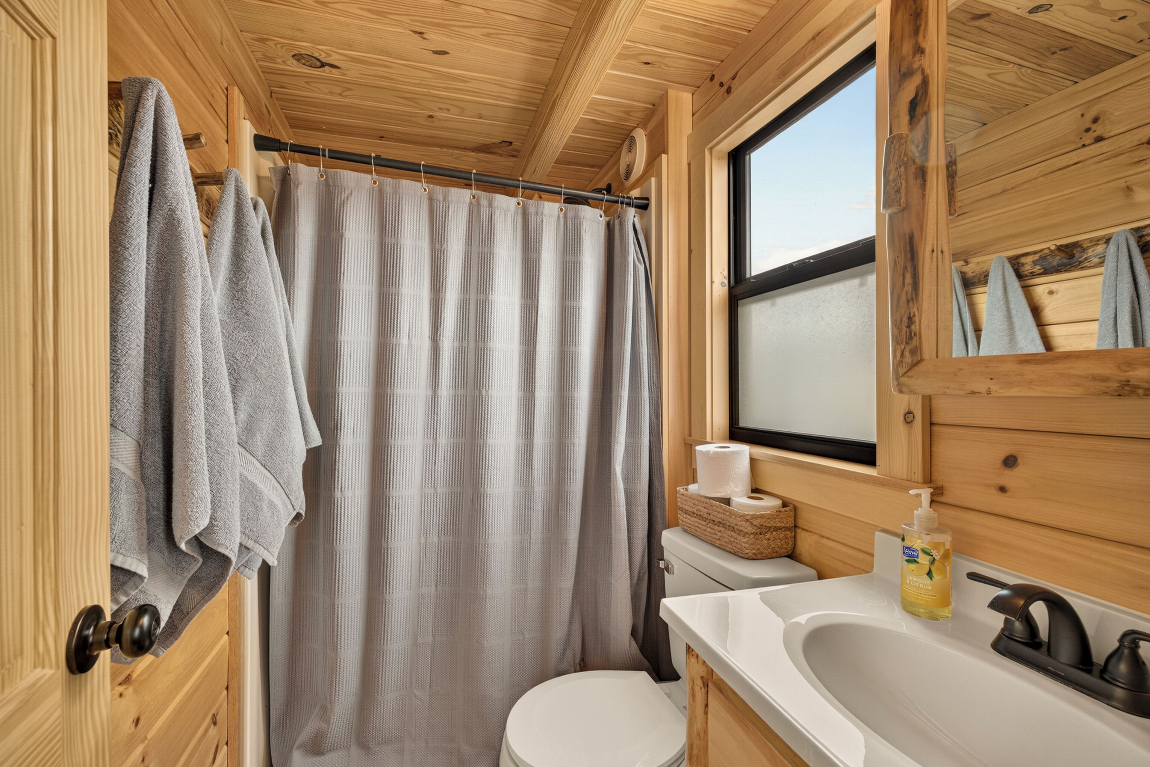 Puisesta mökistä löytyy kylpyhuone, jossa on suihkuverho, wc, pesuallas, jossa on saippua-annostelija, ja ikkuna.