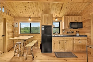 A wooden cabin interior with a kitchen area, including a refrigerator, sink, and wooden cabinets.