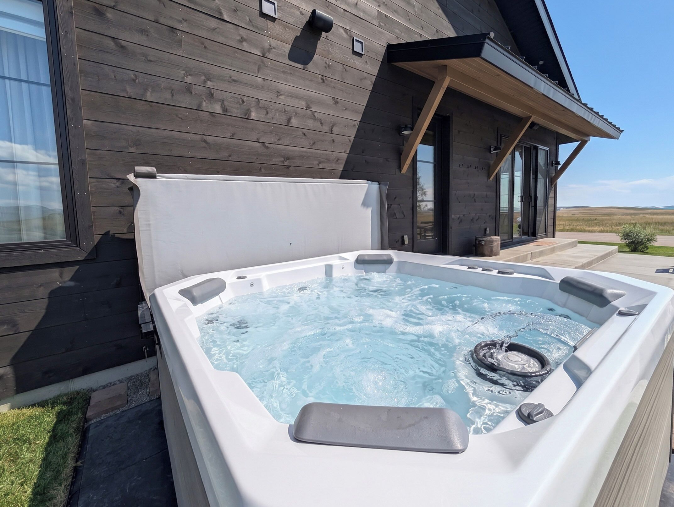Un jacuzzi frente a una casa de madera con vistas despejadas del paisaje.