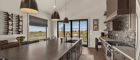 A modern kitchen with a large island, pendant lighting, and a view of the outdoors.