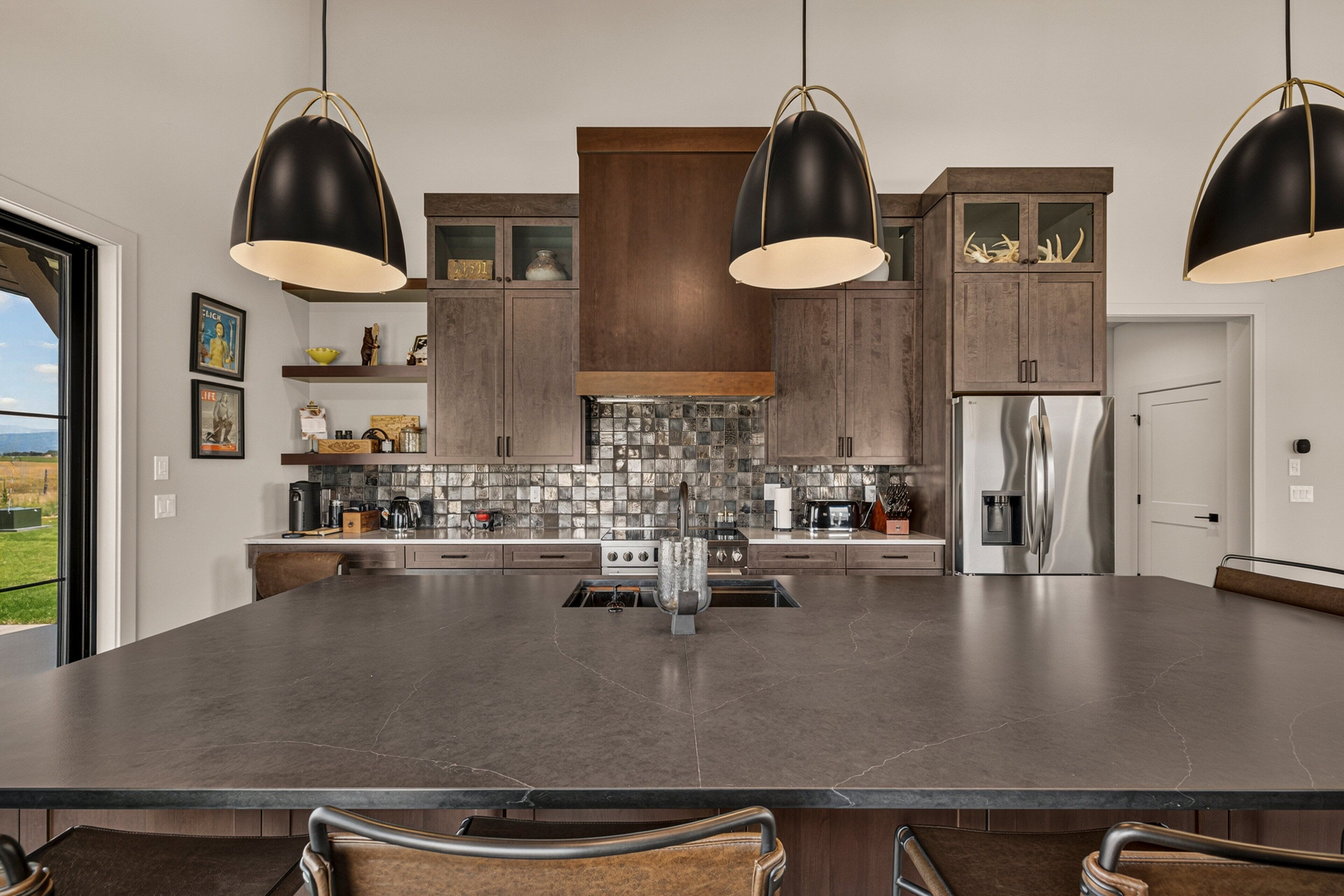 Uma cozinha moderna com uma ilha grande, bancadas escuras e iluminação pendente.