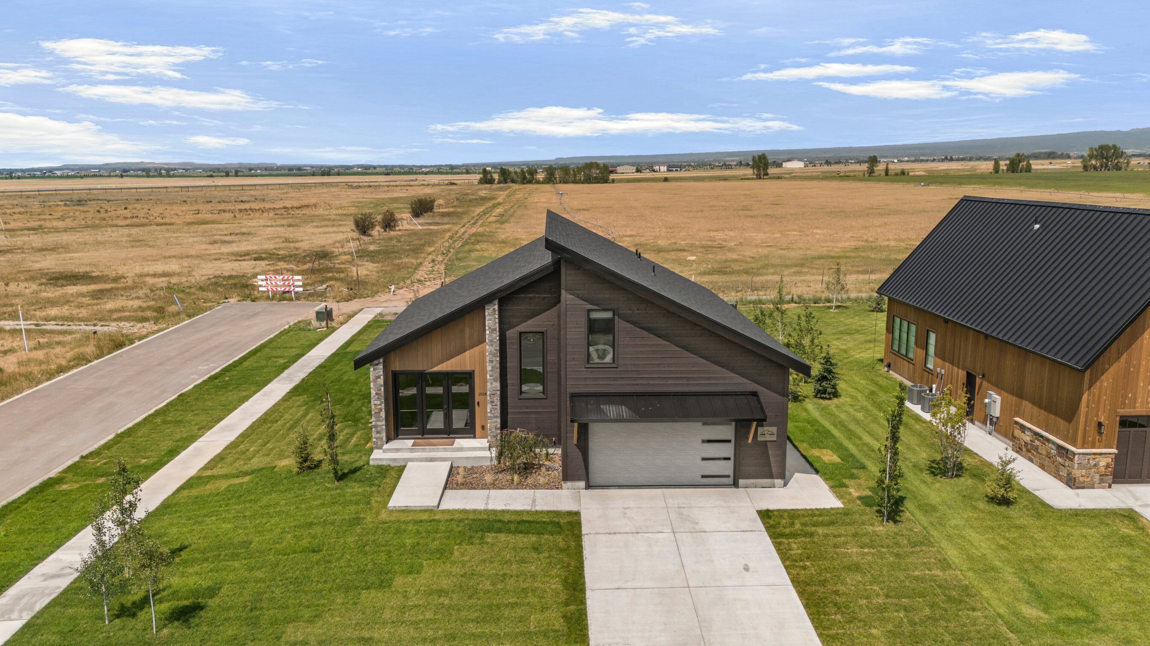 Une maison moderne à deux étages, dotée d’un garage, entourée d’une pelouse bien entretenue et d’un paysage rural.