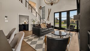 A spacious living area with a staircase, a chandelier, and a view through large windows.