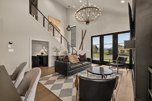 A spacious living area with a staircase, a chandelier, and a view through large windows.
