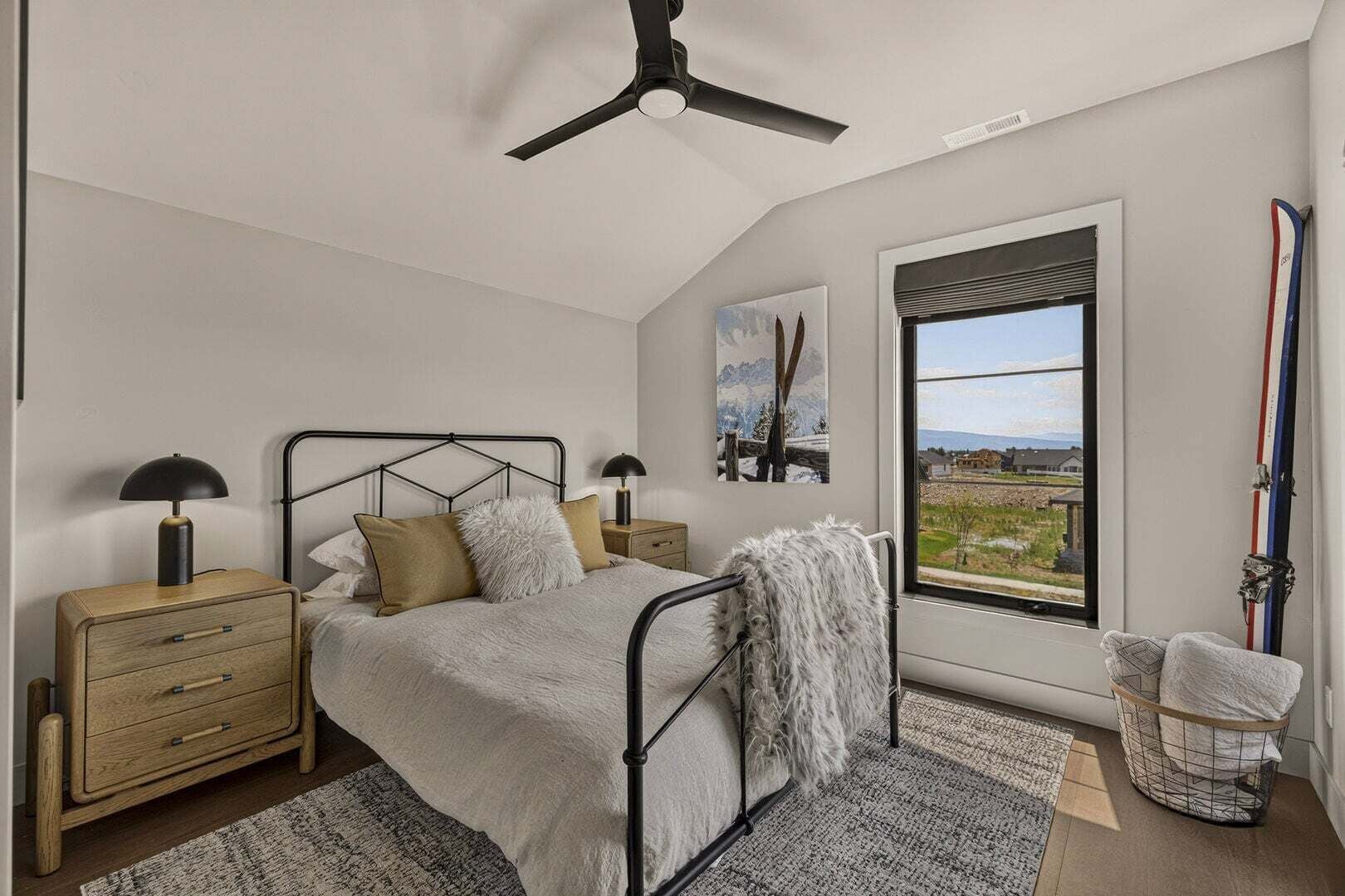A bedroom with a bed, nightstands, a ceiling fan, a window with a view, and a ski rack.