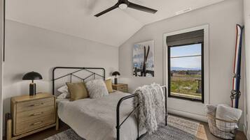 A bedroom with a bed, nightstands, a ceiling fan, a window with a view, and a ski rack.