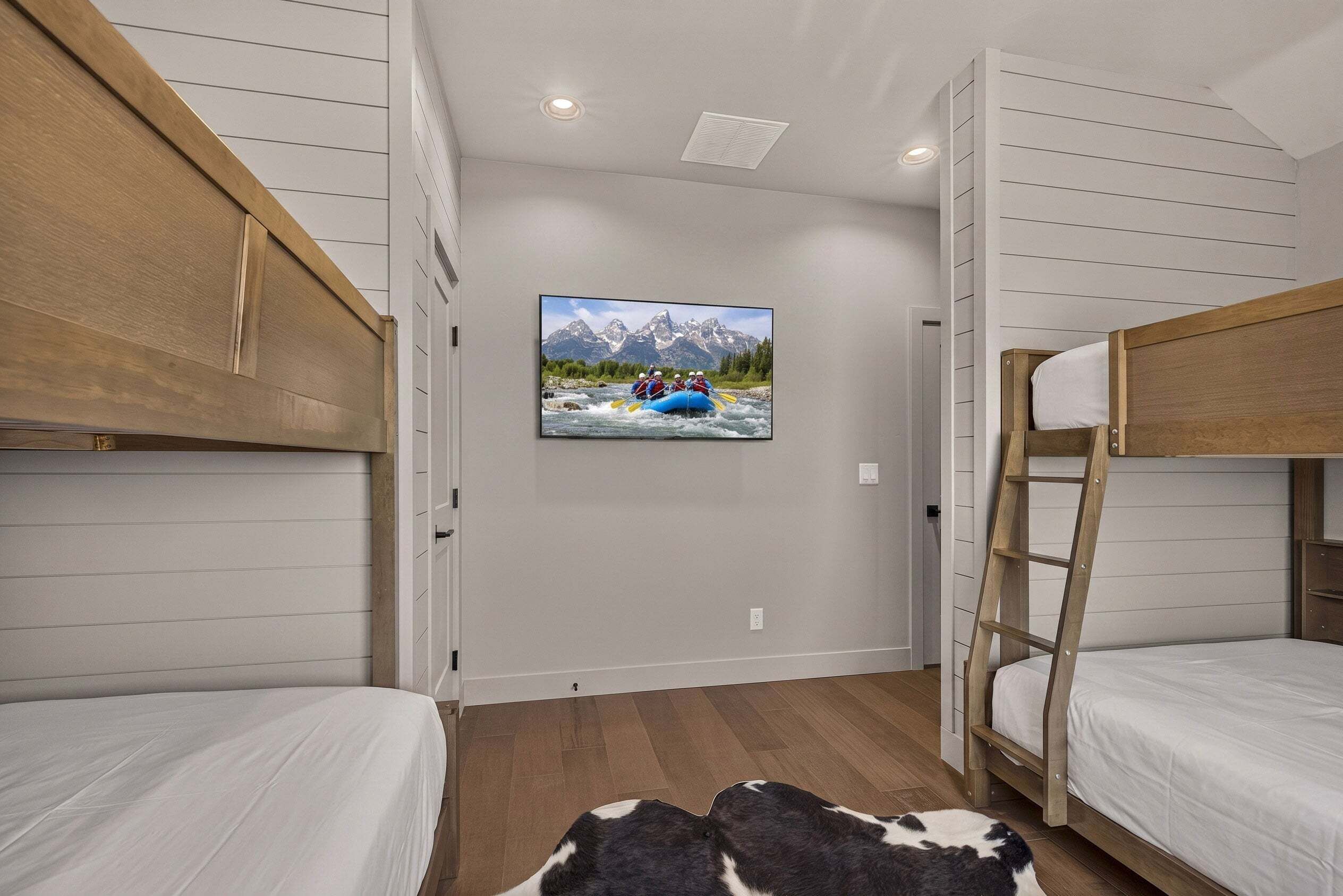 Une chambre avec des lits superposés, un téléviseur fixé au mur qui diffuse une image de paysage de montagne et une échelle en bois.