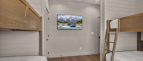 Une chambre avec des lits superposés, un téléviseur fixé au mur qui diffuse une image de paysage de montagne et une échelle en bois.