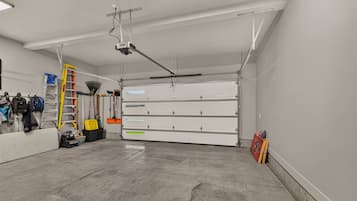 Uma garagem limpa e bem iluminada, com uma grande unidade de armazenamento branca, um projetor montado no teto e diversas ferramentas e equipamentos.